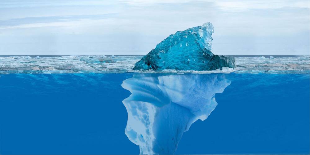 Iceberg sobra a água transparente, evidenciando evidenciando todo o bloco de gelo submerso.