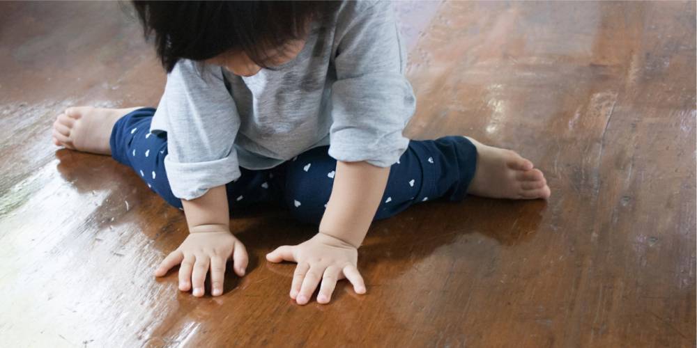 Criança sentada com as pernas em W e as mão apoiadas para a frente.